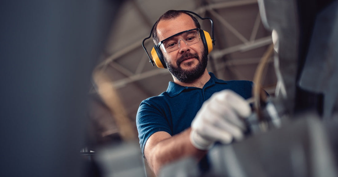 An upward view of a man with yellow hearing protection, white gloves, and safety glasses using equipment.