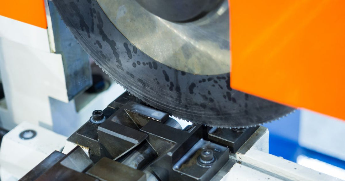 A large circular saw blade is attached to a device with an orange guard. The blade is lowering to cut through a steel bar.
