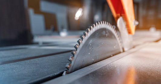 Close-up of a circular metal saw blade with sharp, jagged edges on a shiny, reflective saw table.