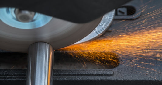 A fast-moving circular saw blade is cutting through a metal pipe. Orange sparks are flying off toward the right.