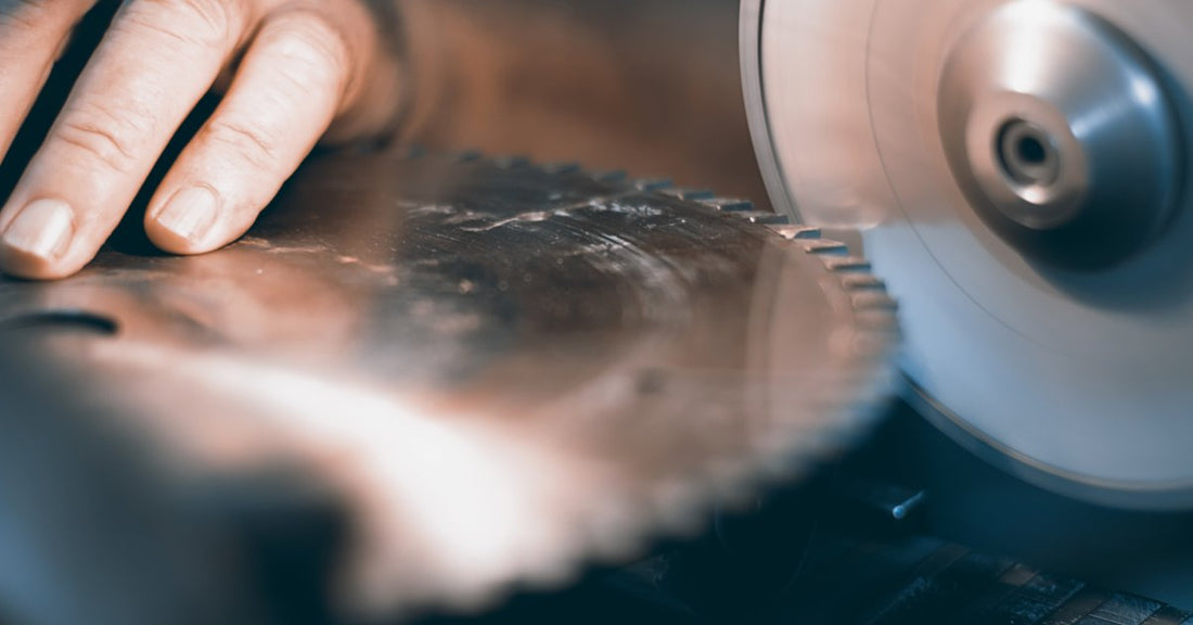 A pair of hands carefully guiding a circular saw blade. They move the blade's teeth against a grinder.