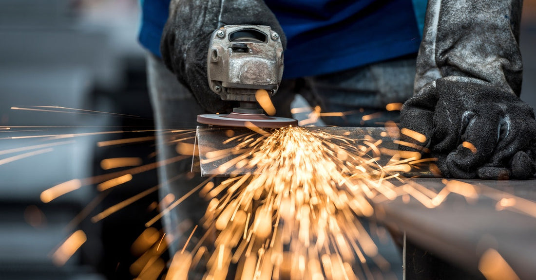 An industrial worker uses an angle grinding saw to cut metal. Sparks are flying off of the piece of metal.