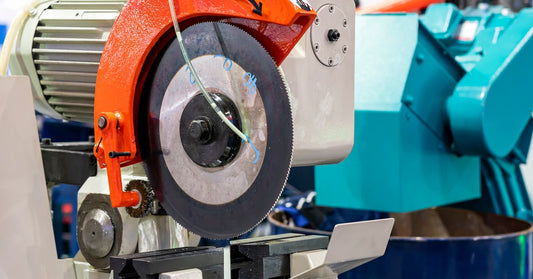 A closeup of a precision metal cutting circular saw. The saw has an orange guard around the edge of the blade.