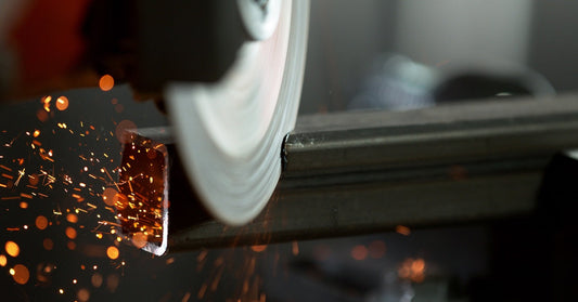 A very close up shot of a metal saw blade spinning very fast and cutting through a square piece of metal.