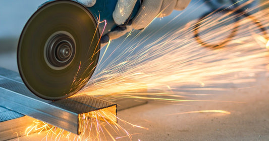 A closeup of an angle grinder being used by two gloved hands. Sparks are flying in the air behind the blade.