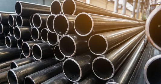 A large stack of aluminum pipes that are piled on top of one another sitting in a large steel warehouse.