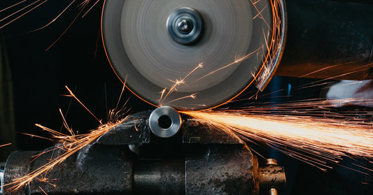 A spinning circular saw blade above a piece of metal. The blade is cutting into it and sending out sparks.