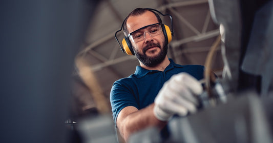 An upward view of a man with yellow hearing protection, white gloves, and safety glasses using equipment.