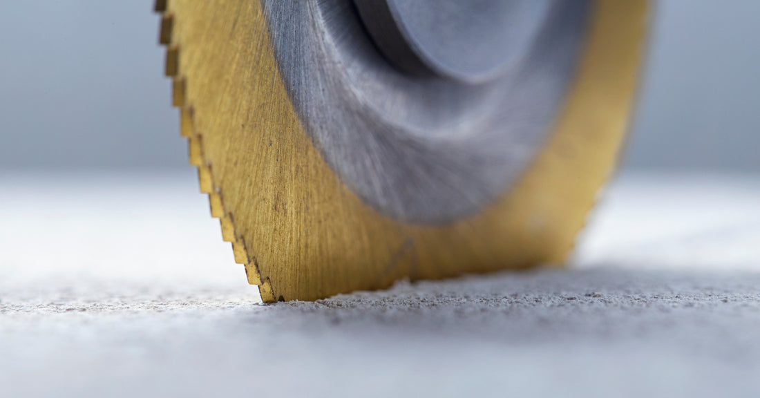 A round metal saw blade with a distinct golden cover around the edge. The blade is cutting into a thick sheet of metal.