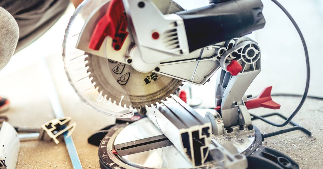 A miter saw with a circular blade loaded into it. A pair of hands are lowering the blade toward a piece of metal.