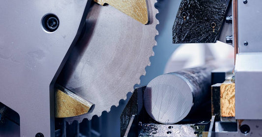 A circular metal cutting saw blade with tipped edges rests next to a round piece of steel that has been cut cleanly.