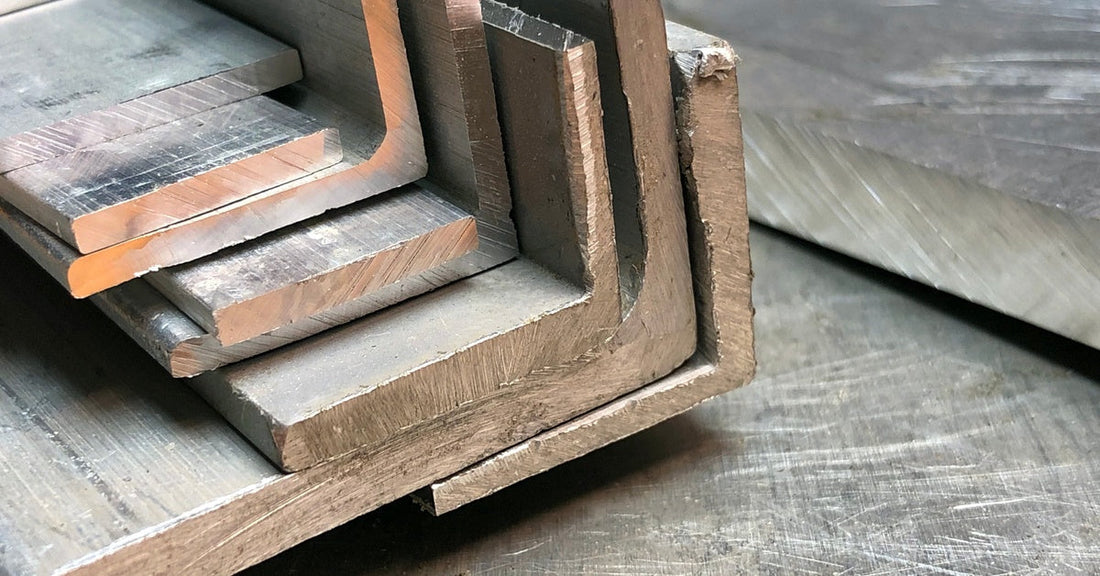 Several thick aluminum corner pieces sit stacked on top of each other on a metal table with scratches on it.