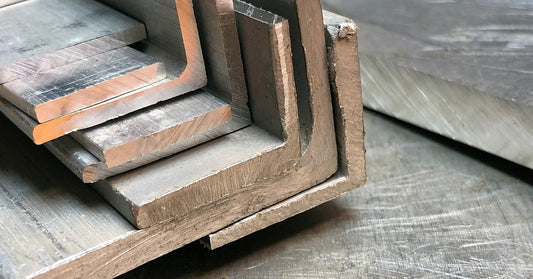 Several thick aluminum corner pieces sit stacked on top of each other on a metal table with scratches on it.